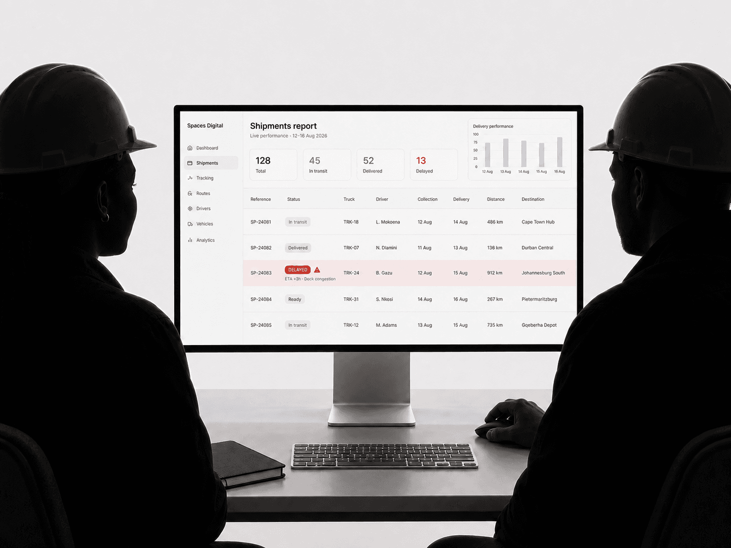 Two silhouetted site logistics managers in safety helmets reviewing a bright Spaces shipments report in a professional studio
